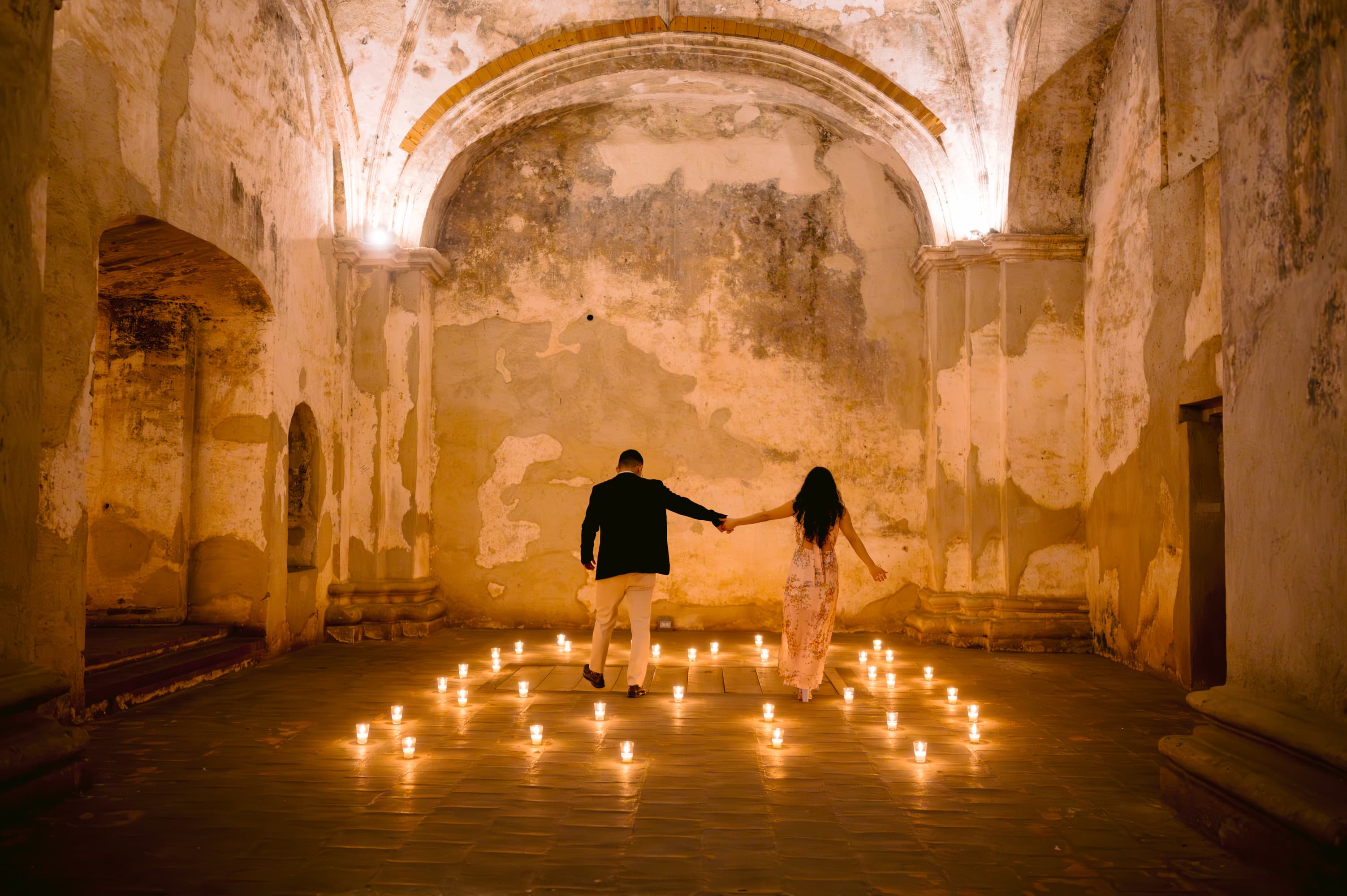 Oscar y Meli caminando de la mano entre cientos de velas, en una antigua nave colonial de Antigua Guatemala.